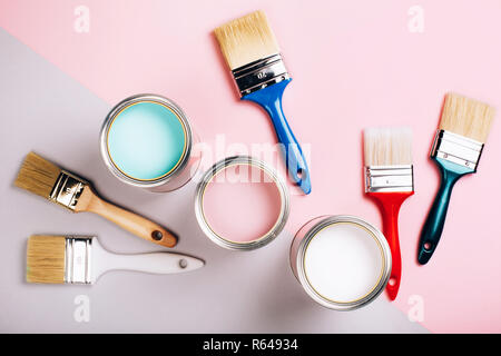 Three open cans of pastel paint with five brushes on pink and grey background. Renovation concept. Stock Photo