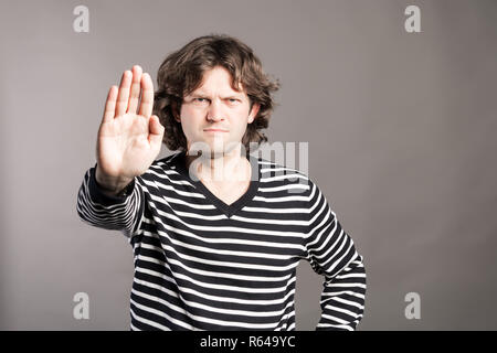 A man shows the hands stop timeout. Male in black and white sweater showing rejective hand gesture, isolated on grey background. Brows furrowed dissat Stock Photo