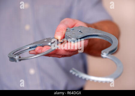 A man holds open handcuffs in his outstretched hand. Close up. Stock Photo