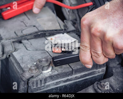 Man recharging a dead car battery in winter time using start-charger. Close up hands of a man with two contact clips from battery charger for vehicles. People under bonnet with starter cables Stock Photo