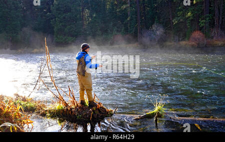 A morning mist rises from the Metolius River in the Cascade Mountains of Oregon, while a fly fisherman casts for rainbow trout in the cold water. Stock Photo