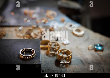 Gold ring on old workbench in an authentic jewelry workshop, in the background other gold jewelery for processing Stock Photo