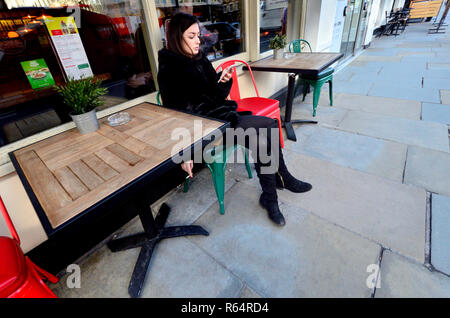 Young woman in black on her mobile phone outside a cafe, London, England, UK. Stock Photo