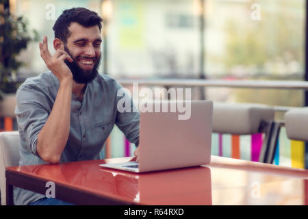 Half length portrait of successful bearded designer smiling at camera while working on freelance at netbook. Stock Photo