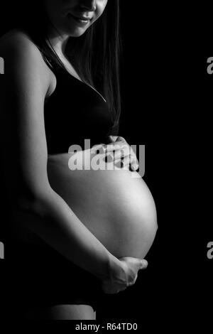 Pregnant woman caressing her belly isolated on black monochrome background. Stock Photo