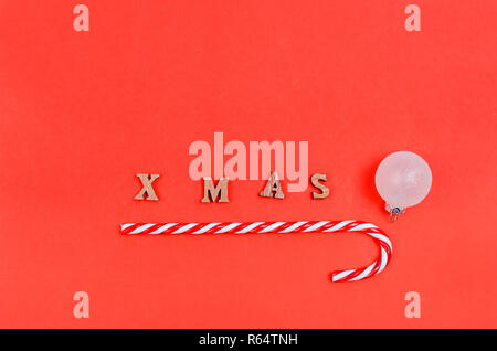 Christmas candy, white ball and the inscription from wooden letters XMAS on a red background, holiday concept, copy space Stock Photo
