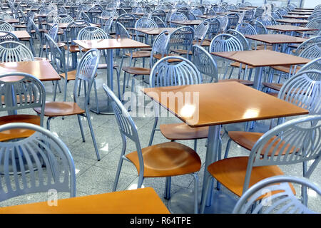 Many brown square eating tables and metal chairs staying in empty cafe hall inside high modern building Stock Photo