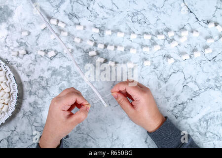 Diy marshmallow garland. Guide on photo how to make a decorative marshmallow garland, threads, needles and branches with your own hands. Handmade Chri Stock Photo