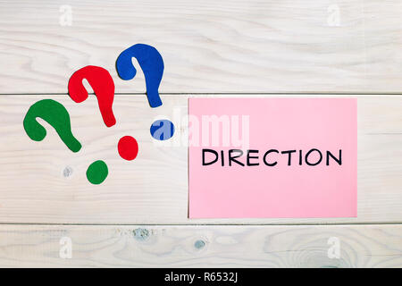 Word direction and question marks on wooden table, which way to go in business concept. Stock Photo