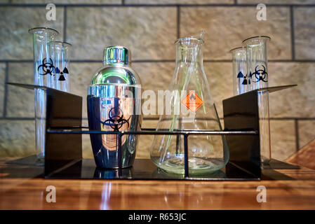 Shaker, flask and test tubes with the symbol of biological hazard, flammable liquid and radiation on a metal rack. Stock Photo