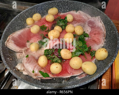 Pan cooking slices of swordfish, seasoned with fresh parsley leaves, new potatoes, pepper. The cooking moves the slices, a bit of steam rises from the Stock Photo