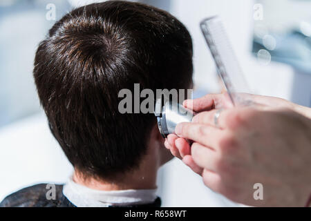 Master cuts hair of men in the barbershop, hairdresser makes hairstyle for a young man. Stock Photo