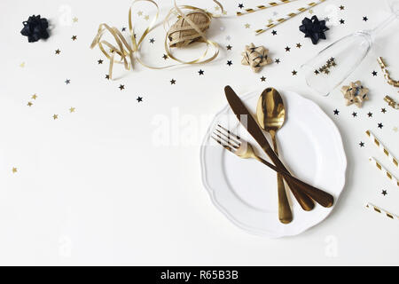 New Year, Christmas styled glamorous black and gold table setting with plate, goldenware, confetti stars and champagne glass. Party decoration, flat lay, top view. Empty space. Restaurant menu concept Stock Photo