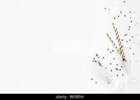 Happy New Year composition. Champagne glasses with golden confetti stars and drinking straws isolated on white table background. Celebration, party concept. Flat lay, top view. Empty copy space. Stock Photo