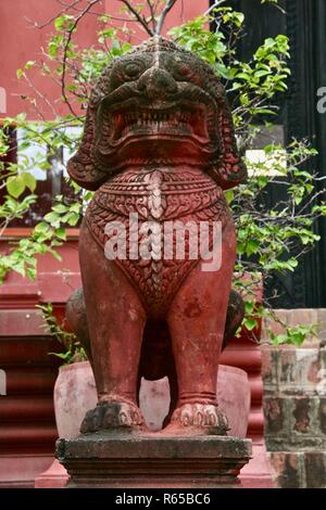 A weathered red lion standing guard in a garden in Cambodia Stock Photo