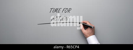 Wide view image of male hand writing a Time for action text on grey background in a conceptual image. Stock Photo