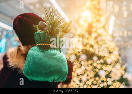 Santa from behind with gift bag on background of bokeh christmas tree. Stock Photo