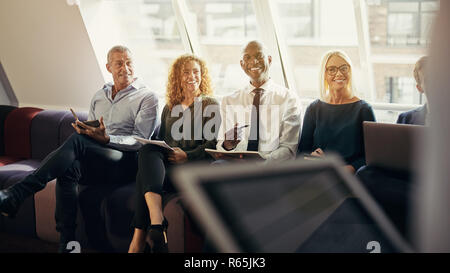 Smiling group of diverse businessmen and businesswomen sitting together on a sofa in an office during a presentation Stock Photo