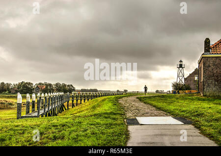 Schokland, The Netherlands, October 24, 2018: Lonesome jogger on a cobble path between the reconstructed harbour and the adjacent mound on the former  Stock Photo