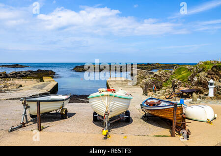 A line of three colorful old wood fishing boats pulled ashore at a small harbor on the rocky coast of Northern Ireland at Dunseverick Harbour Stock Photo