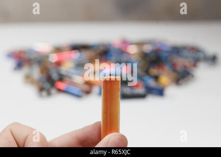 Concept of recycling. Used alkaline battery in hand and a lot of blurred alkaline batteries in the background. Stock Photo