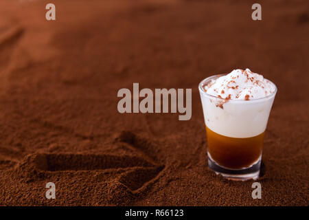 Little cup of piccolo latte macchiato on a table covered with arrow on ground coffee as a background Stock Photo