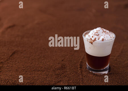 Little cup of piccolo latte macchiato on a table covered with ground coffee as a background Stock Photo
