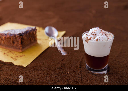 Little cup of piccolo latte macchiato on a table covered with ground coffee as a background and chocolate brownie with cocoa cream and coconut chips Stock Photo
