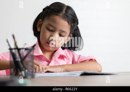 Children use a eraser is deleting words. Close up the little girl is doing homework on the wooden table. Select focus shallow depth of field with copy Stock Photo