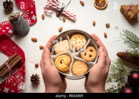 Round box filled with cookies in a woman's hands. Above view of a table full of Christmas goodies and decorations Stock Photo