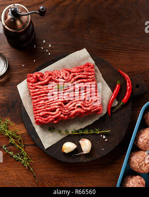 Minced beef meat and meatballs with salt, garlic, herbs on wooden table. Top view. Stock Photo