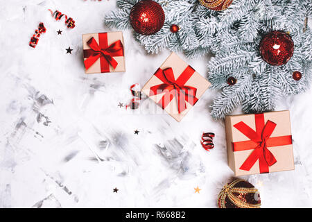 Three present boxes with red bow, christmas balls and snow fir-tree on white concrete background. Place for text. Festive concept. Stock Photo