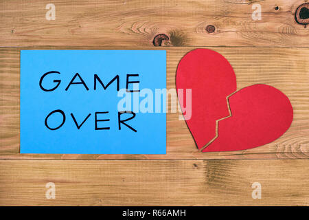 Broken heart and blue paper with text game over on wooden table,relationship breakup concept. Stock Photo