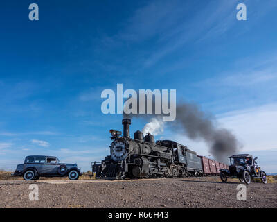 Locomotive 453 steam-engine freight train approaches County Road E5 crossing with a Model-T and a 1933 Dodge waiting by the tracks. Stock Photo