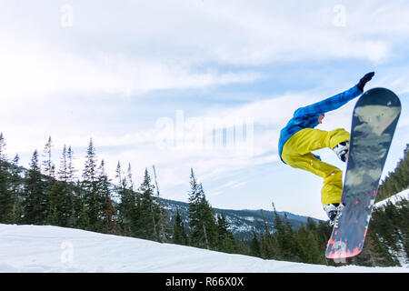 Snowboarder freerider jumping from a snow ramp in the sun on a background of forest and mountains Stock Photo