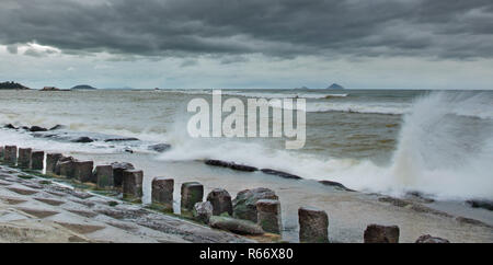 Storm protection concrete coastline defence structure barrier with the ocean beyond and waves hitting the structure. With islands in the background set in the south china sea. Stock Photo