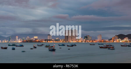 Asian holiday resort Nha Trang Vietnam under a cloudy sunset evening sky from a view point north of the city. With construction development and the city lights ablaze over the fishing boat harbour. Stock Photo
