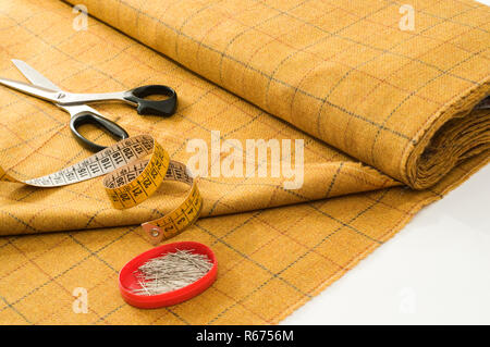 a piece of fabric, scissors, tape measure and pins on the tailor's table Stock Photo