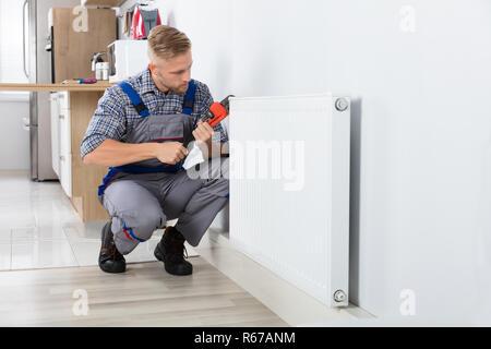 Male Plumber Fixing Thermostat Using Wrench Stock Photo