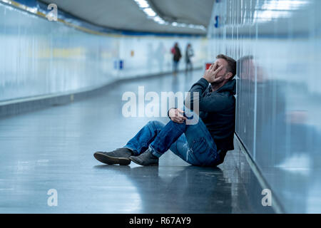 Sad young man crying suffering depression stress sitting on ground street subway tunnel looking desperate leaning on wall alone in Mental disorder Emo