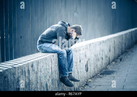 Young attractive man suffering from depression stress sitting alone and sad on the street feeling anxious and lonely in unemployment Mental health Dru Stock Photo