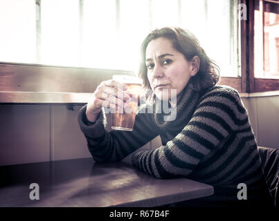 Portrait of a attractive latin woman drinking beer in a bar pub feeling depressed unhappy and lonely in Alcohol Use Abuse Depression and mental health Stock Photo