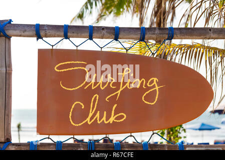 Orange vintage signboard in shape of surfboard with Surfing Club text and palm tree in background Stock Photo