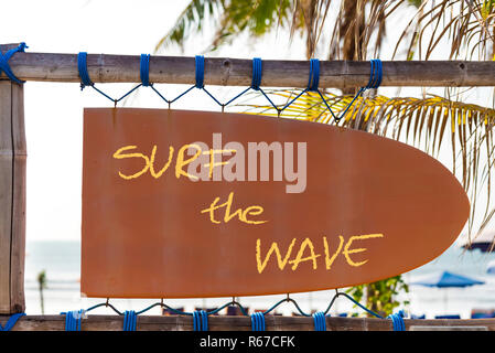 Orange vintage signboard in shape of surfboard with Surf the Wave text and palm tree in background Stock Photo