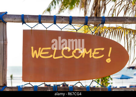 Orange vintage signboard in shape of surfboard with Welcome text and palm tree in background Stock Photo