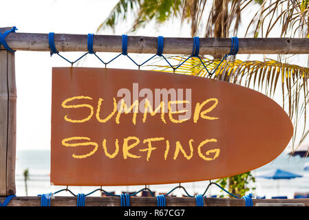 Orange vintage signboard in shape of surfboard with Summer Surfing text and palm tree in background Stock Photo