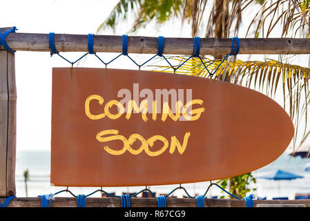 Orange vintage signboard in shape of surfboard with Coming Soon text and palm tree in background Stock Photo