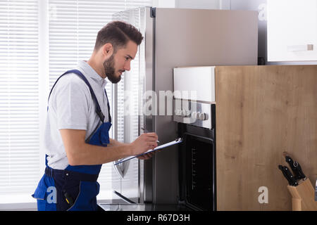 Electrician Writing On Clipboard In Front Of Oven Stock Photo