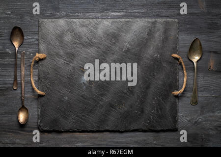 Black slate plate and three vintage spoons on wooden board. Top view, copy space Stock Photo