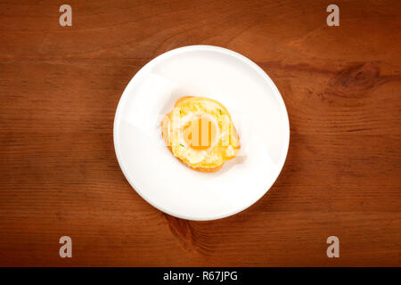 A photo of a quail egg, fried sunny side up, on a cracker, shot from the top on a dark rustic wooden background with a place for text Stock Photo